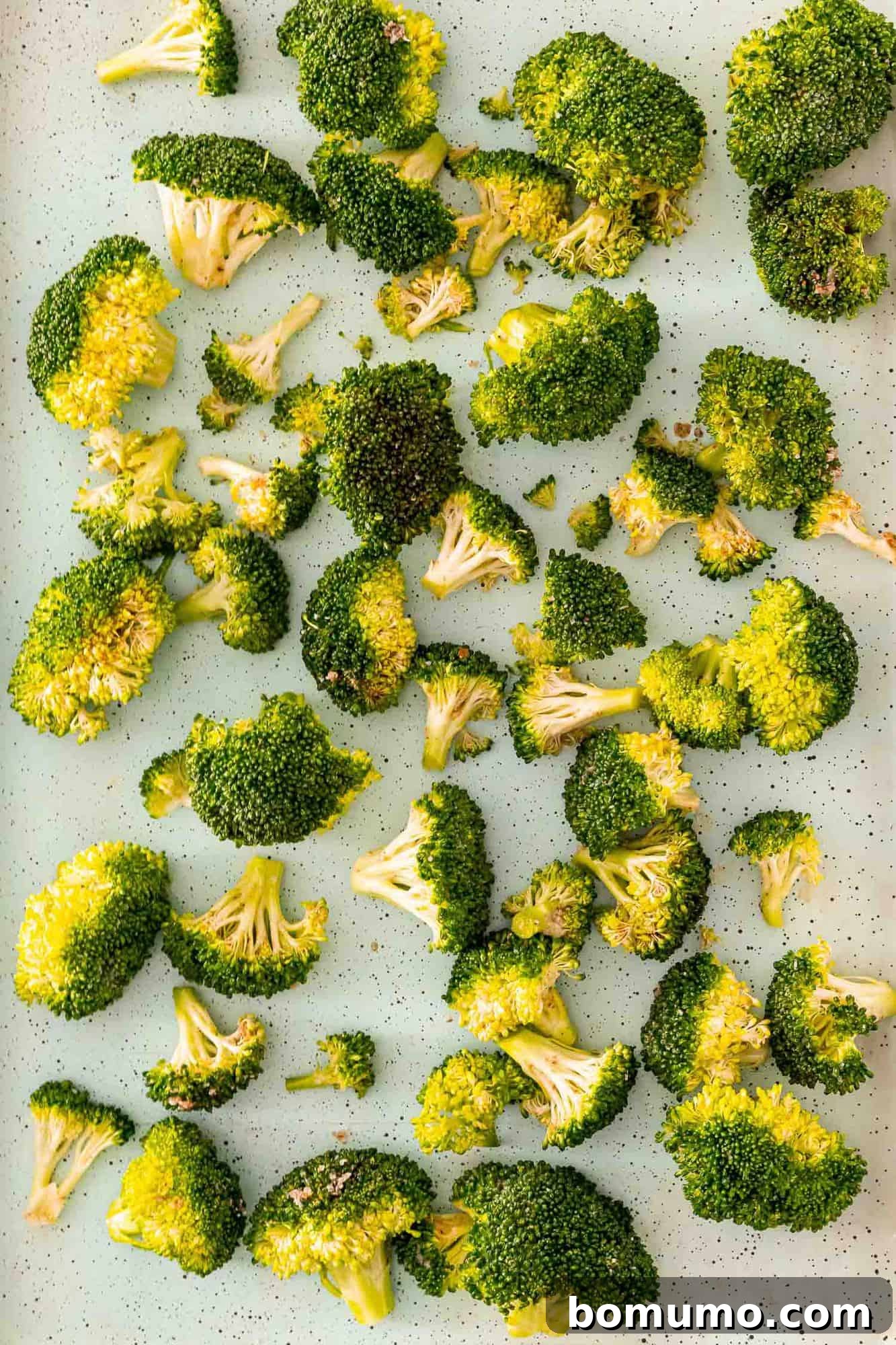 Crispy Lemon-Parmesan Roasted Broccoli 6 Uncooked, seasoned broccoli florets spread out in a single layer on a sheet pan, ready for roasting.