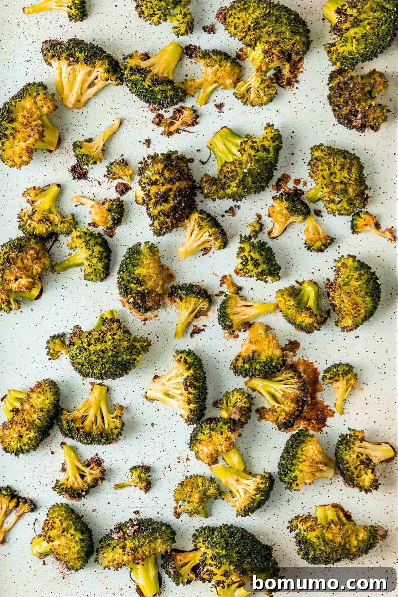 Crispy Lemon-Parmesan Roasted Broccoli 7 Golden-brown, perfectly roasted broccoli florets spread on a parchment paper-lined sheet pan, fresh from the oven.