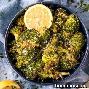 Roasted broccoli with lemon and parmesan in a dark blue bowl.