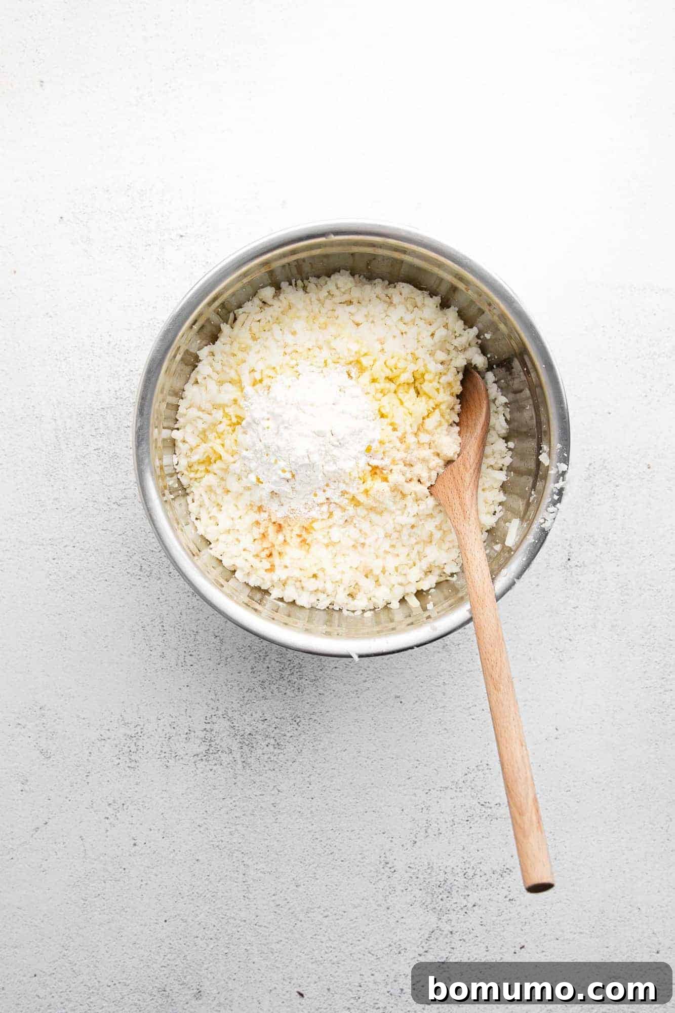 Close-up of uncooked hash browns mixed with seasonings in a large white mixing bowl, ready for shaping.