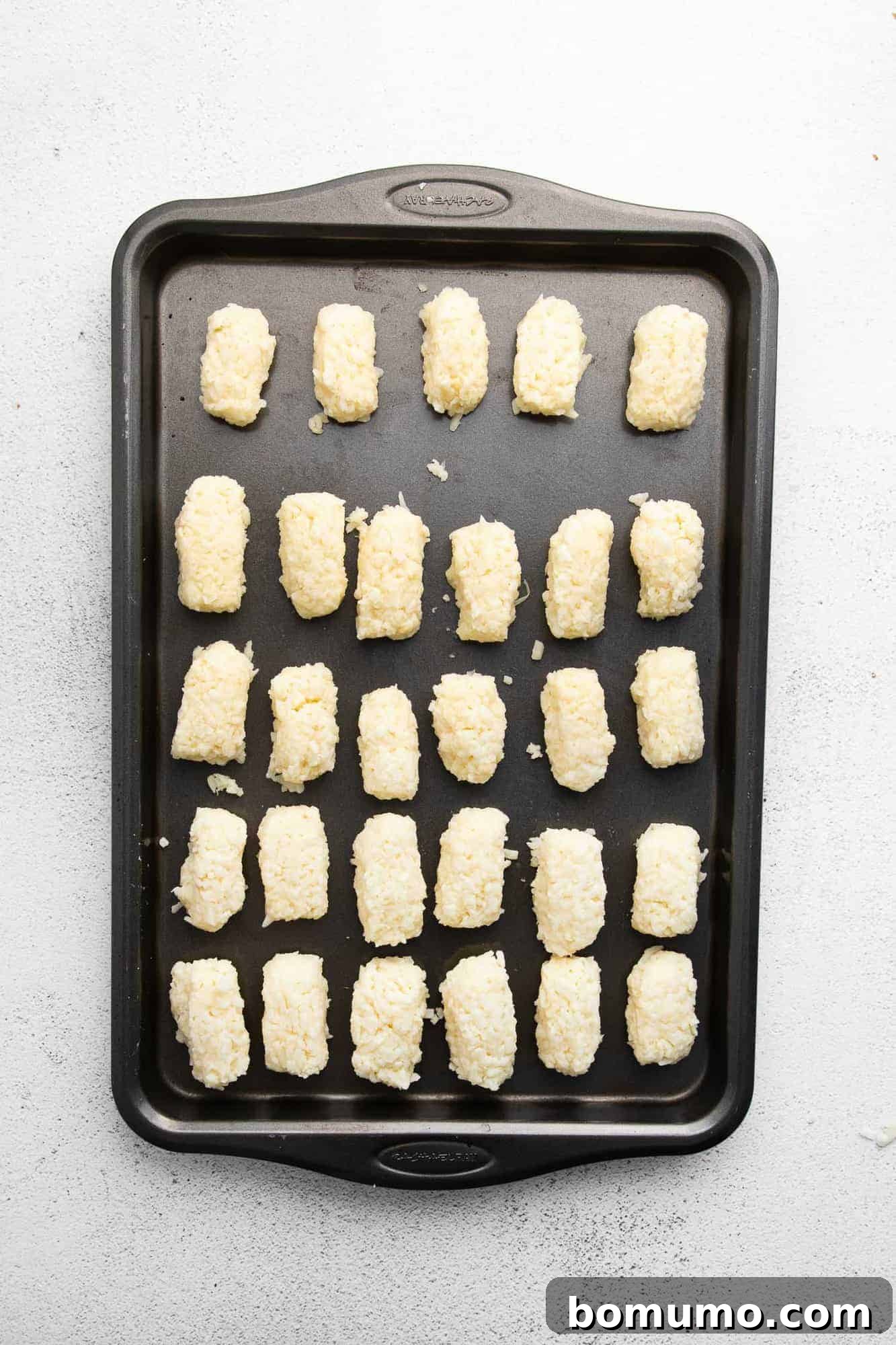 Neatly arranged rows of uncooked homemade tater tots on a baking sheet, ready for the air fryer.