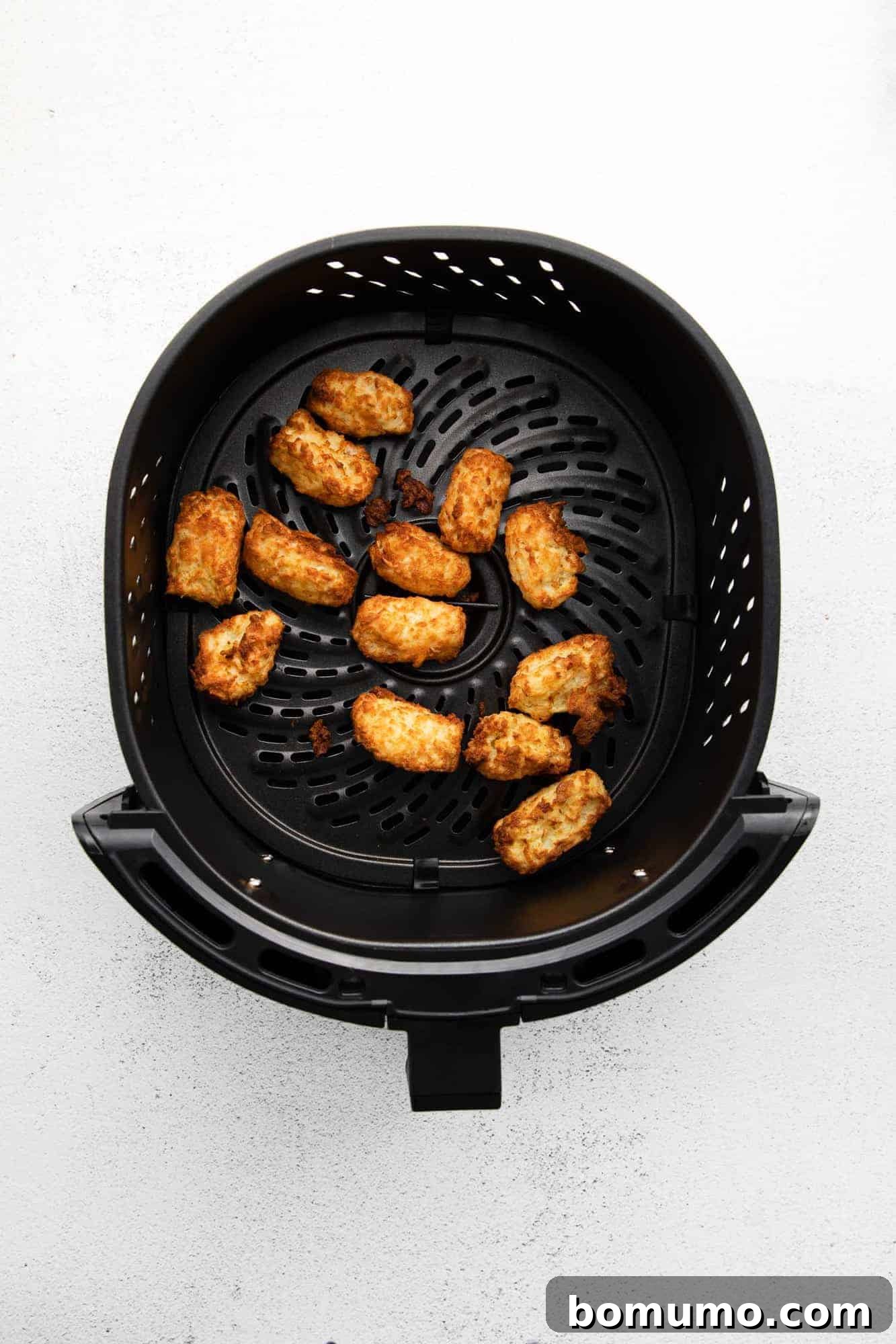 Hot and crispy cooked air fryer tater tots still in the air fryer basket, steam visibly rising, indicating their fresh warmth.
