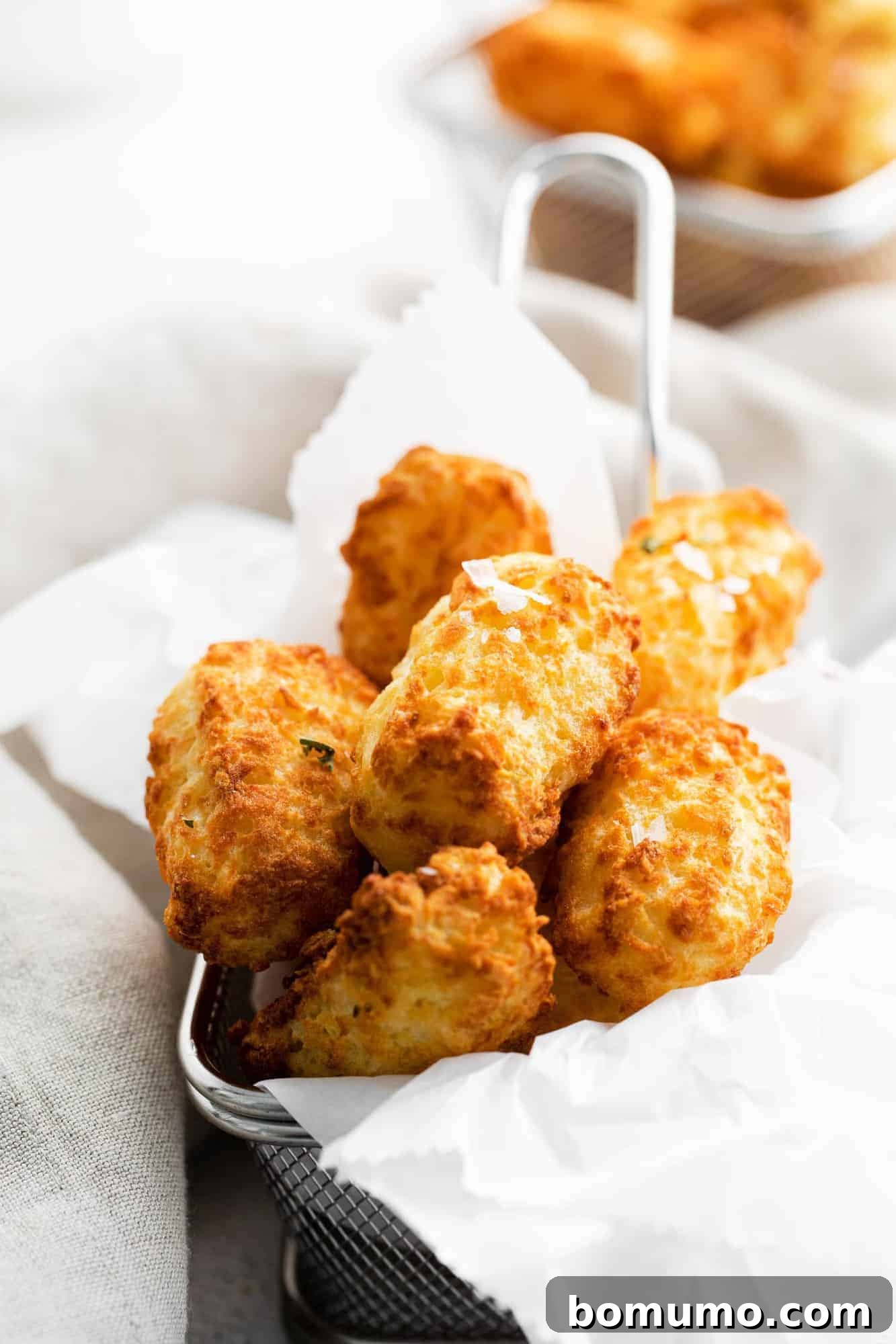 Close up of individual crispy air fryer tater tots presented in a tiny metal fryer basket, showcasing their perfect texture and golden color.