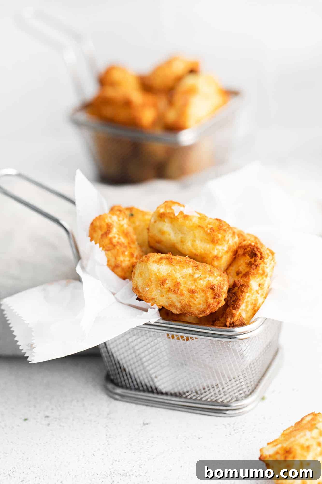 A small metal basket lined with parchment paper, filled with an abundant pile of perfectly golden and crispy air fryer tater tots.