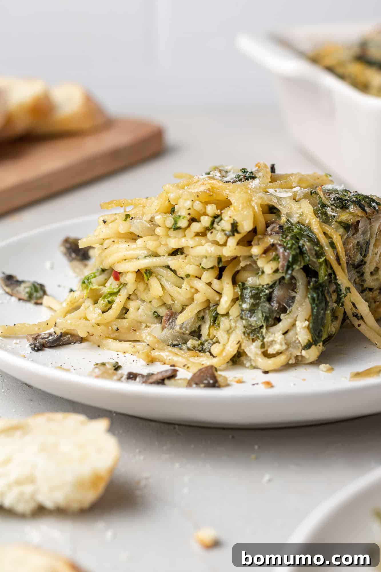 Cheesy Spinach Baked Spaghetti 11 Close up of spaghetti mixed with spinach, cheese, and mushrooms on a small white plate.