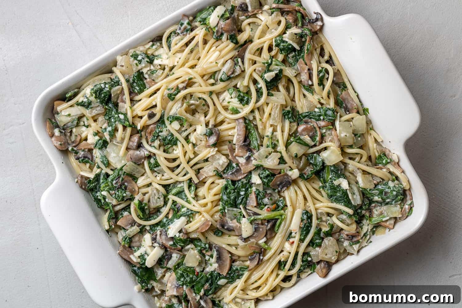 Cheesy Spinach Baked Spaghetti 7 Unbaked spaghetti with spinach and mushrooms in a square white baking dish.