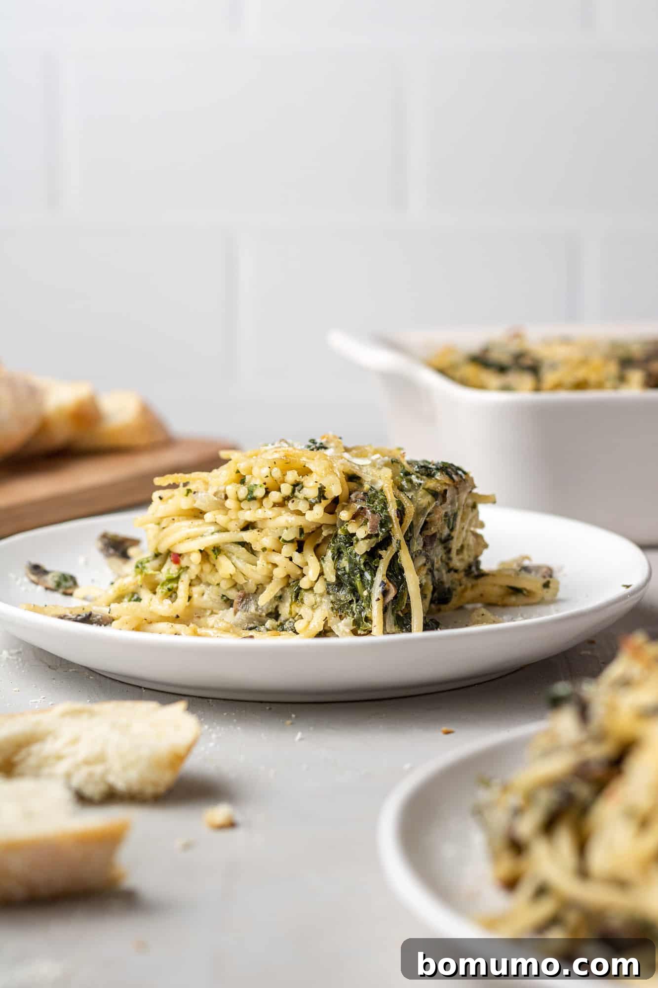 Cheesy Spinach Baked Spaghetti 10 Square of baked spaghetti on a plate with casserole dish in the background.