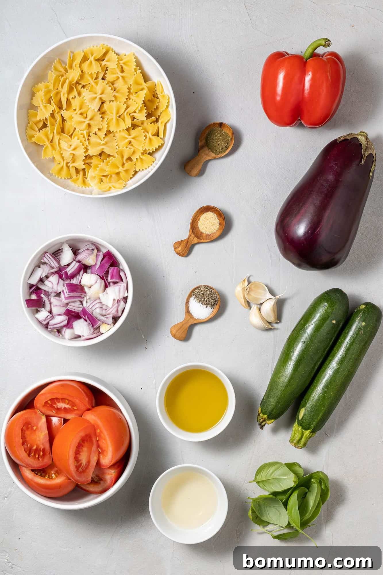 Fresh vegetables, cooked pasta, and dressing ingredients on a gray background.