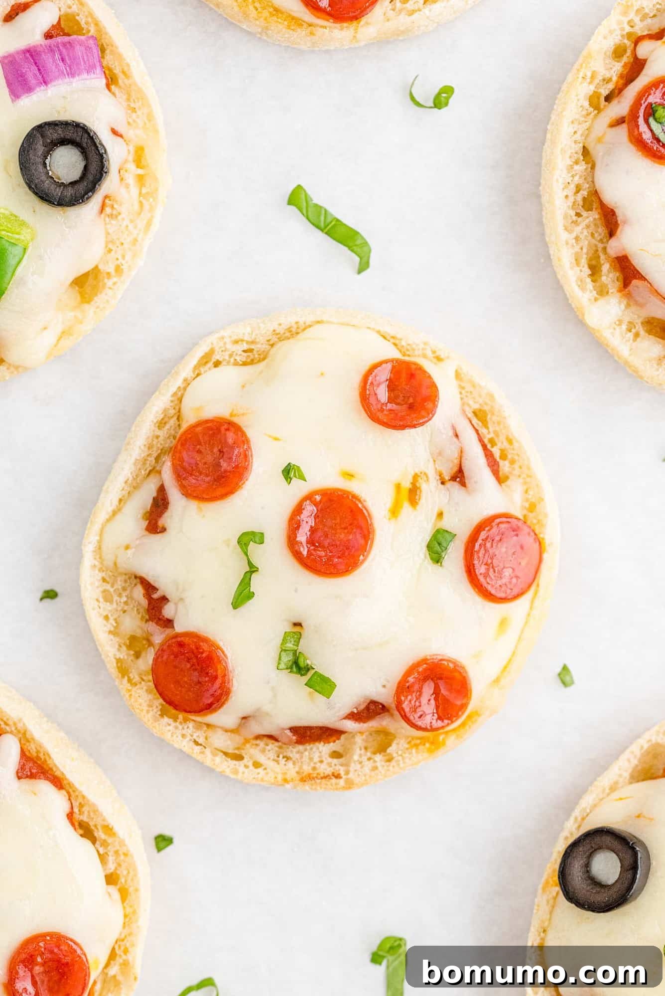 Overhead view of a pepperoni English muffin pizza, others partially visible, showcasing a golden-brown crust and melted cheese.