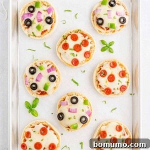 Overhead view of English muffin pizzas on a parchment paper lined baking sheet, ready to be served.