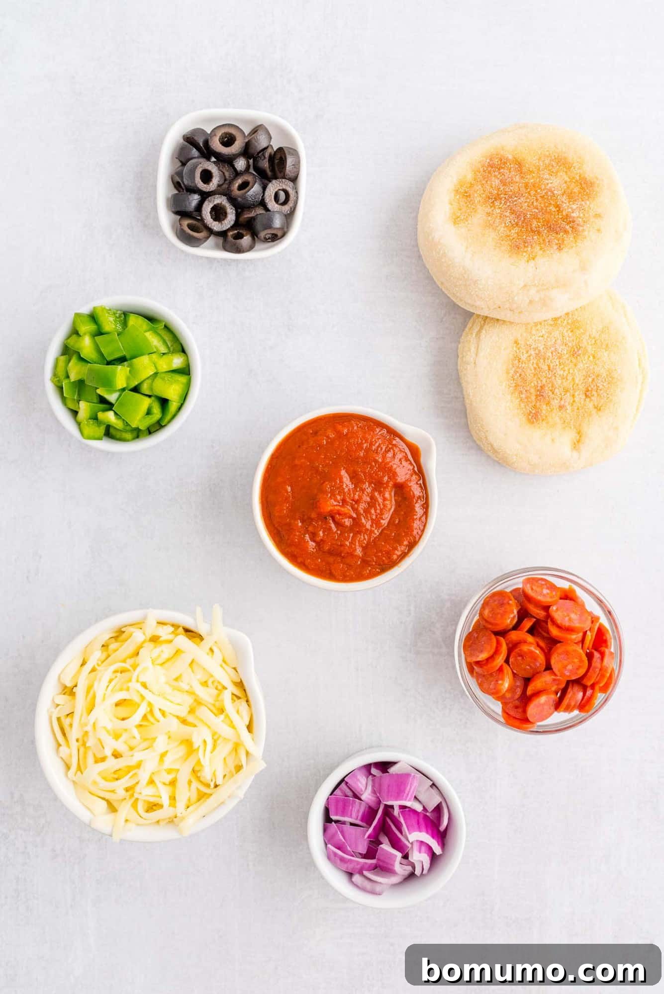 Overhead view of ingredients needed for English Muffin Pizzas: English muffins, a jar of pizza sauce, and shredded mozzarella cheese.