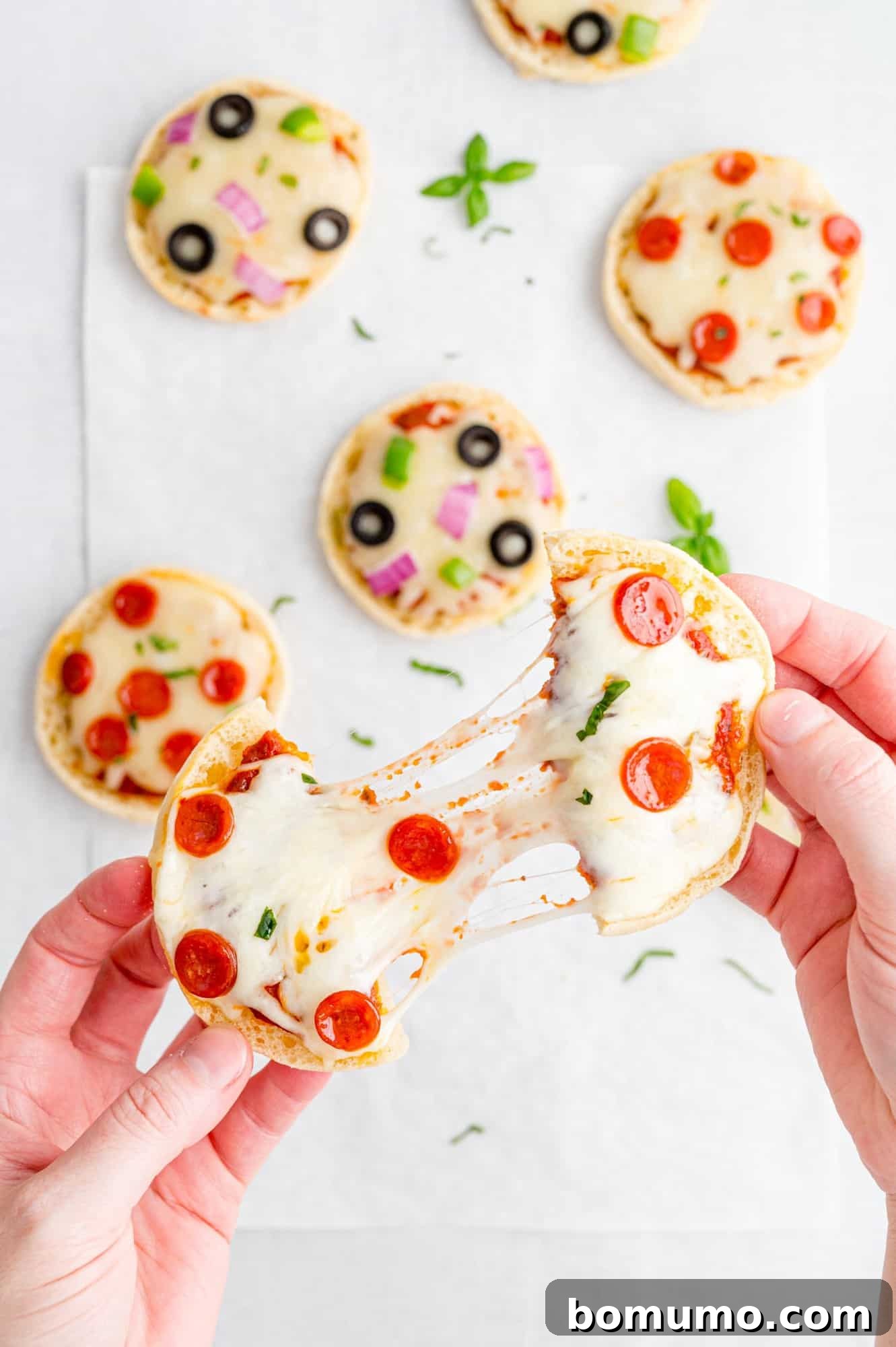 Two halves of an English muffin pizza being pulled apart, with melted cheese stretching between them, indicating a perfectly cooked and delicious outcome.