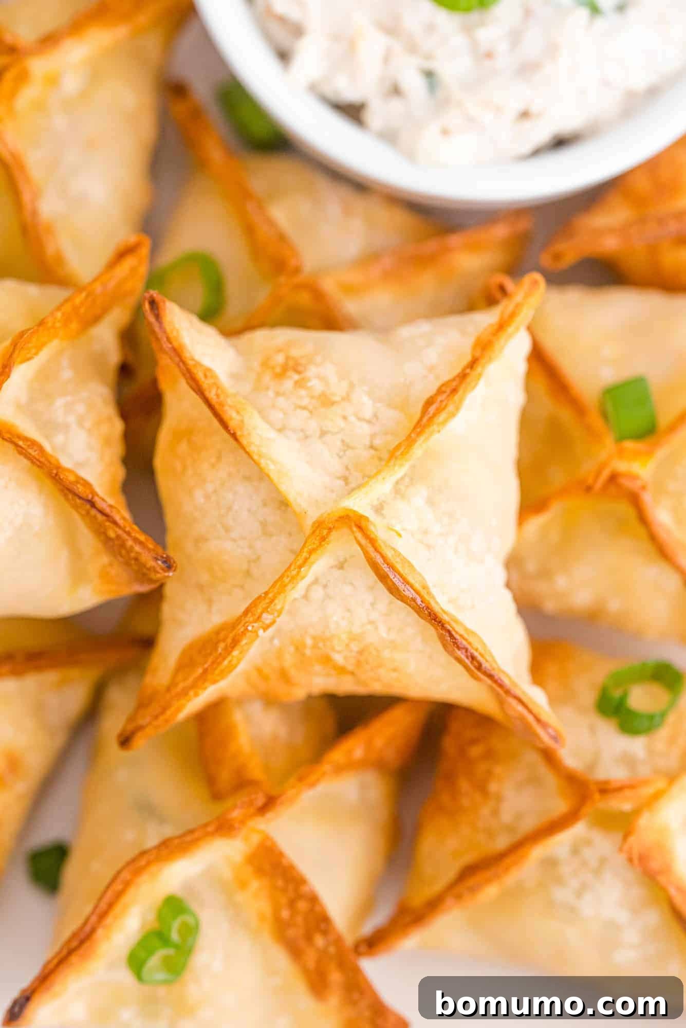 A stack of golden brown air fryer crab rangoon on a white plate, garnished with chopped green onions.