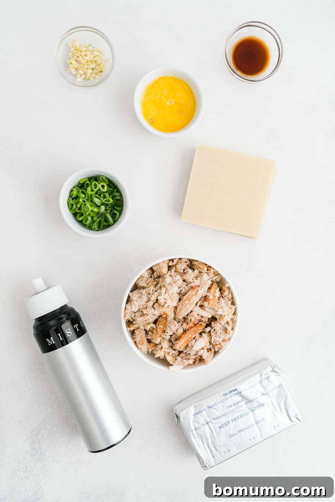 Overhead view of fresh ingredients including cream cheese, crab meat, green onions, and wonton wrappers.
