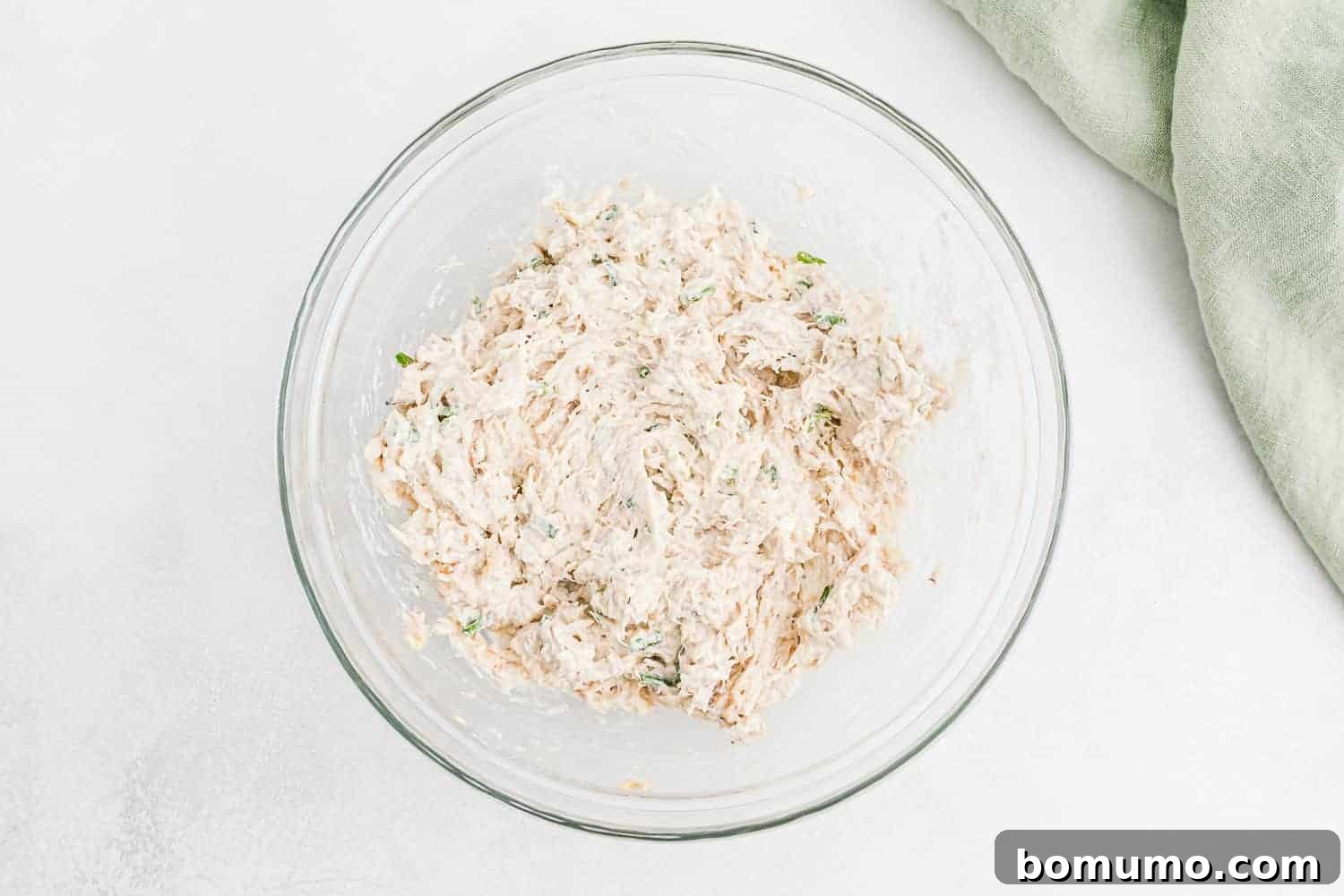 Creamy crab rangoon filling in a clear glass mixing bowl, ready for assembly.