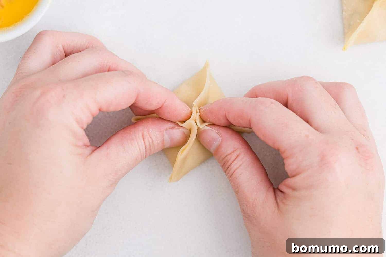 Two hands are shown working together to fold a crab rangoon, emphasizing the communal aspect.