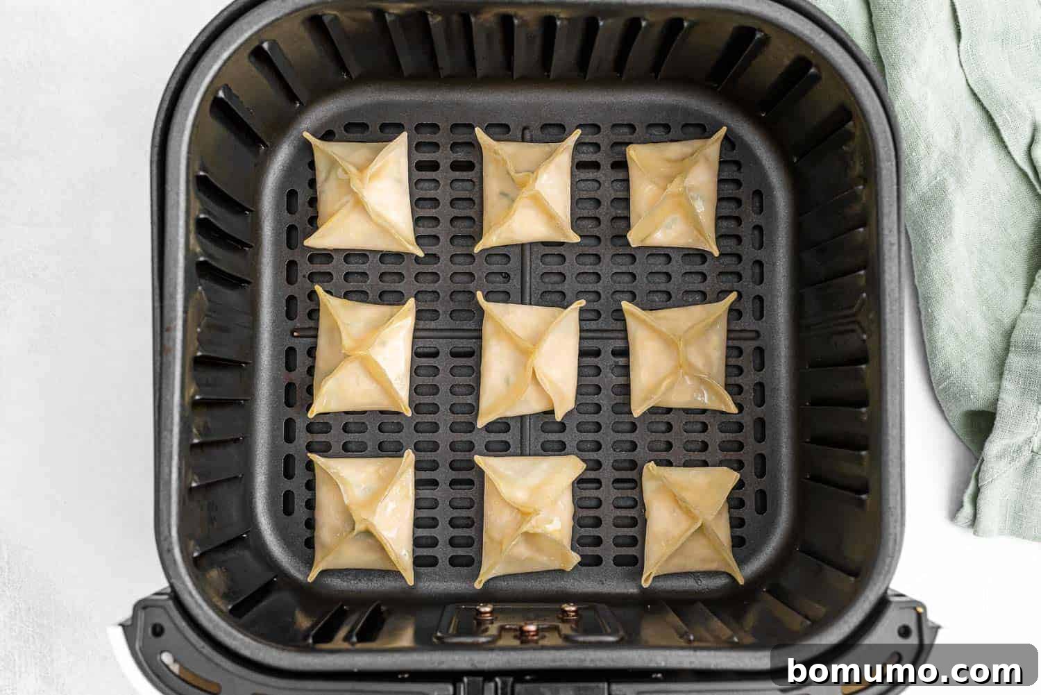 Golden brown crab rangoon cooking in an air fryer basket, showing a perfect single layer.