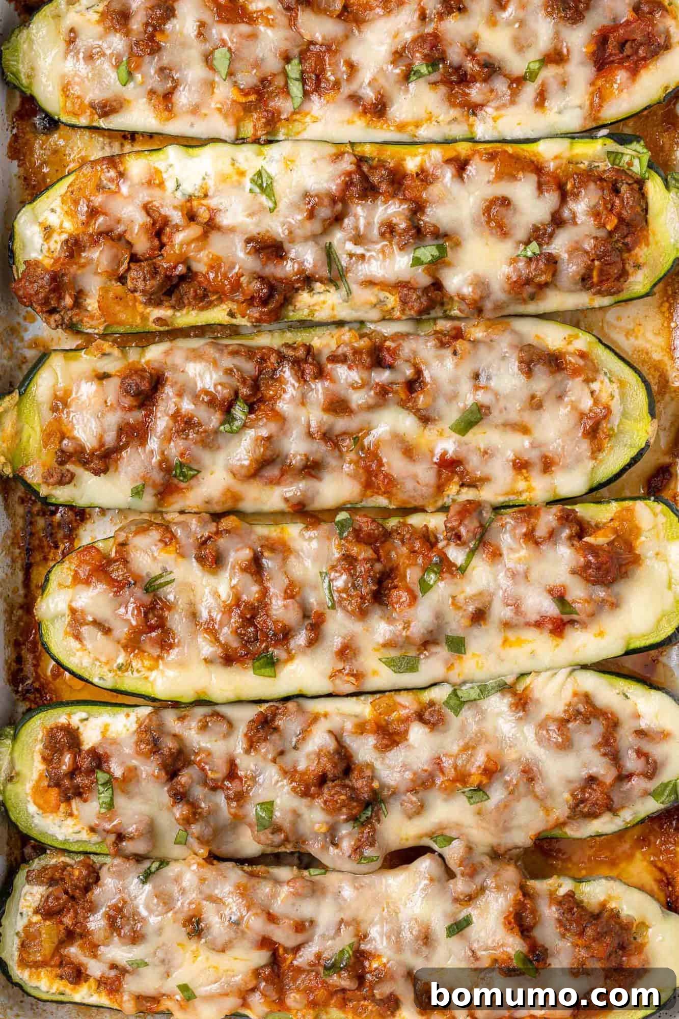 Overhead view of zucchini halves lined up and stuffed with ricotta and meat sauce.