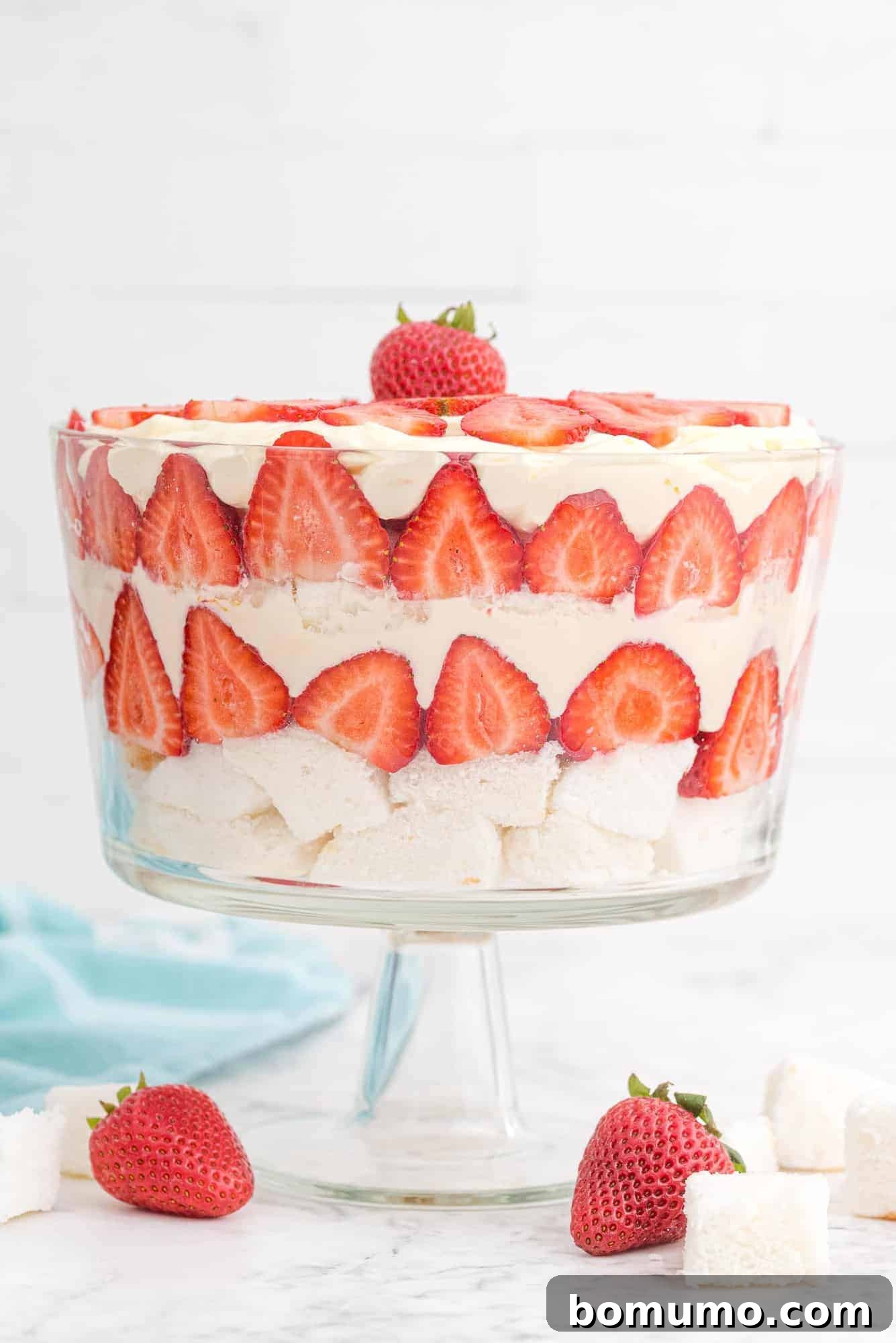Effortless Strawberry Trifle 2 Vibrantly layered strawberry trifle in a clear glass trifle bowl, set against a pristine white background. Each layer of cake, strawberries, and cream is distinct and inviting.