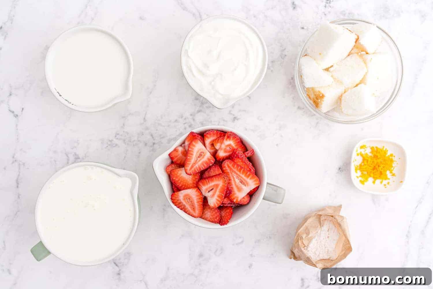 Effortless Strawberry Trifle 4 An overhead shot showcasing all the fresh ingredients neatly arranged for making a strawberry trifle, including a whole angel food cake, a bowl of strawberries, milk, yogurt, and other components.