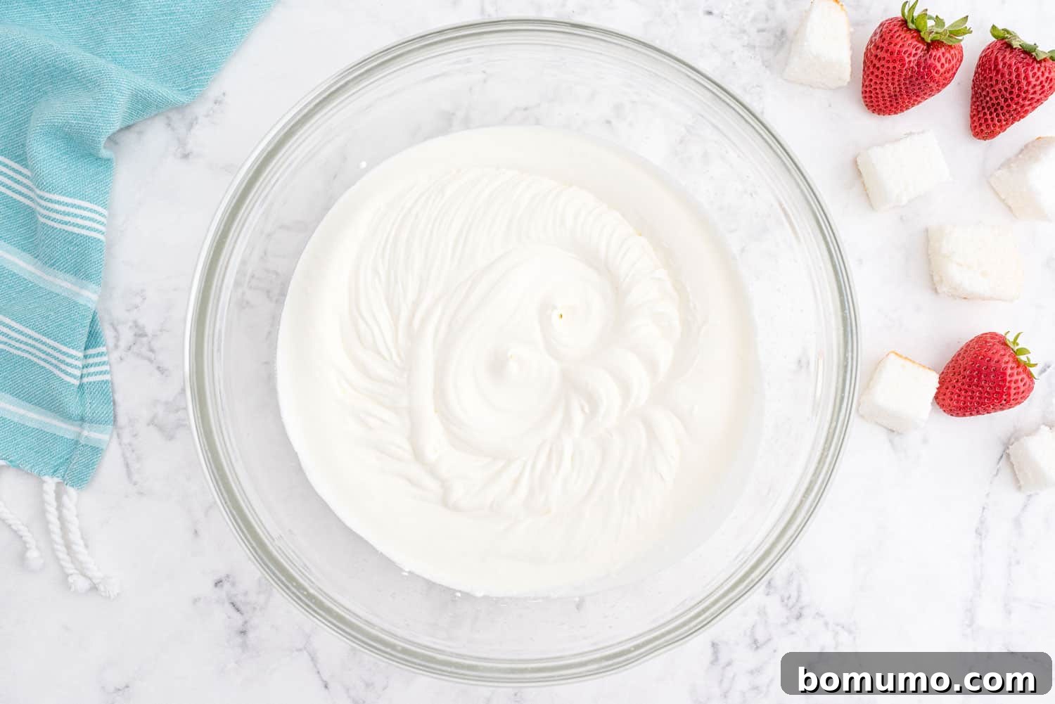 Effortless Strawberry Trifle 7 Fluffy, stiffly beaten whipped cream in a clear glass mixing bowl, showcasing its perfect texture.