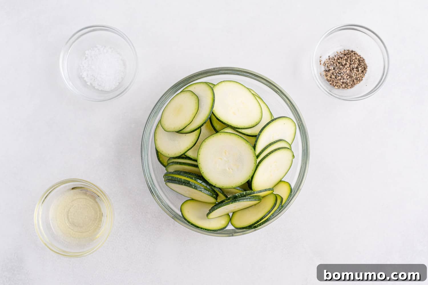 Overhead view of ingredients needed to make recipe: thinly sliced zucchini, a bottle of olive oil, salt, and pepper.