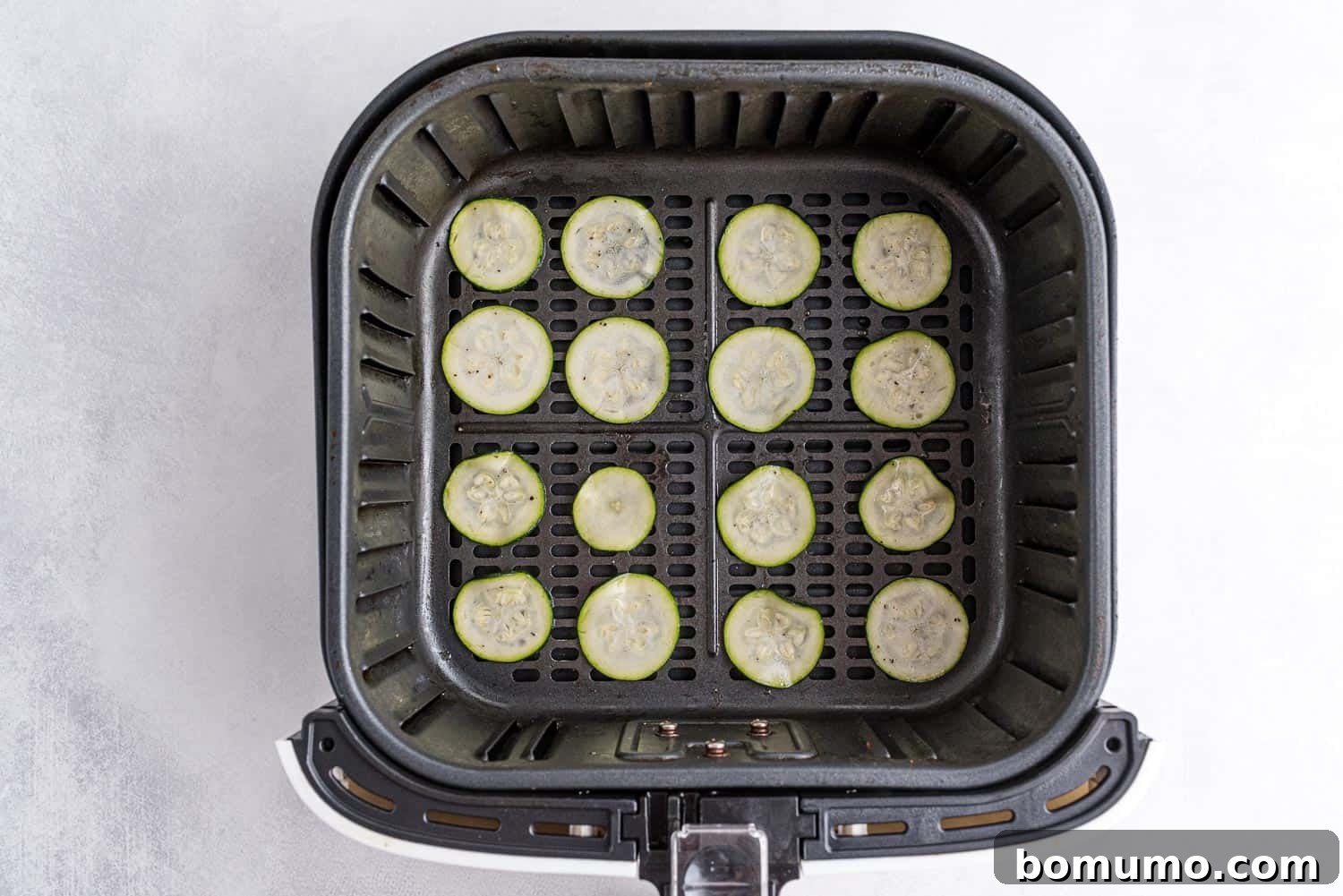 Thinly sliced and seasoned zucchini arranged in a single layer within the basket of an air fryer, ready for cooking.