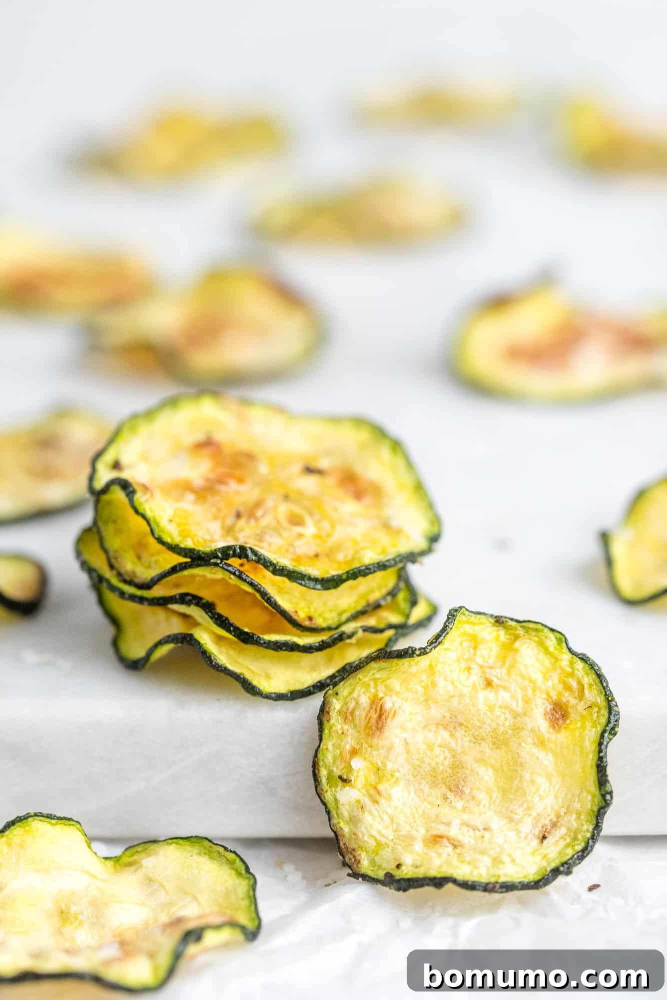 Thinly sliced, cooked zucchini chips artfully arranged on a clean white background, showcasing their light and crispy texture.