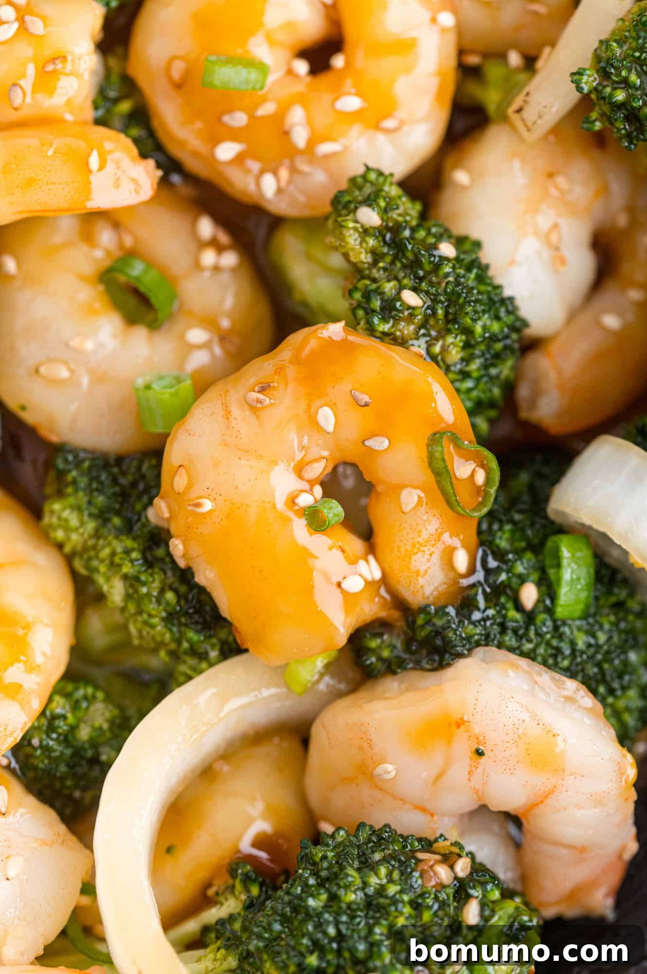 Close-up of succulent shrimp and vibrant green broccoli coated in a rich, glossy brown stir-fry sauce, garnished with toasted sesame seeds.