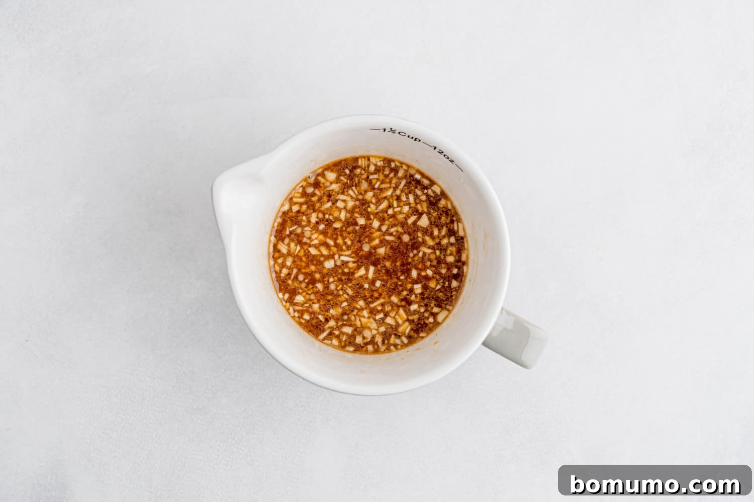 Small white measuring cup filled with the whisked brown sauce ingredients, ready for cooking.