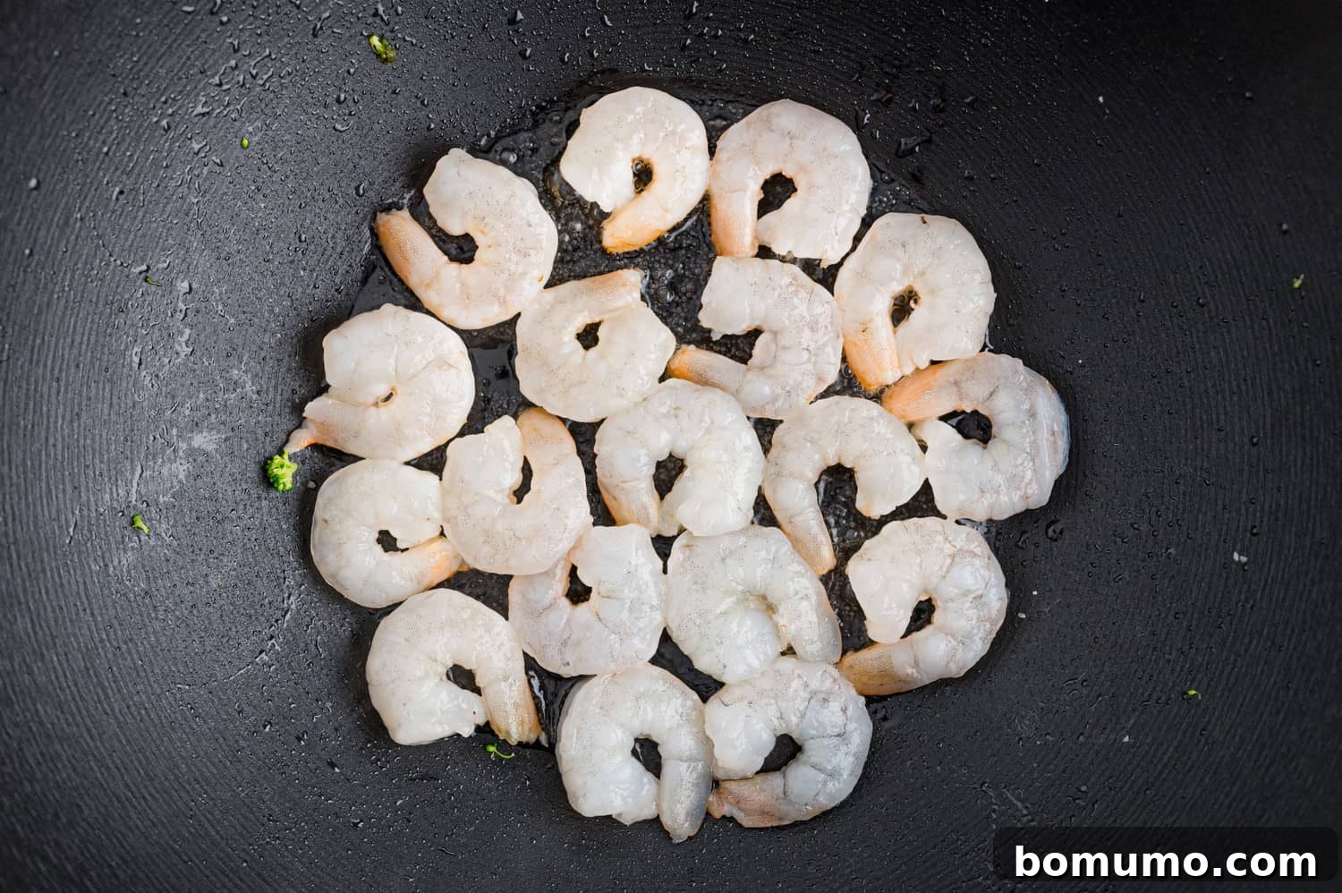 Raw, uncooked shrimp laid out in a single layer in a hot black frying pan, ready for searing.