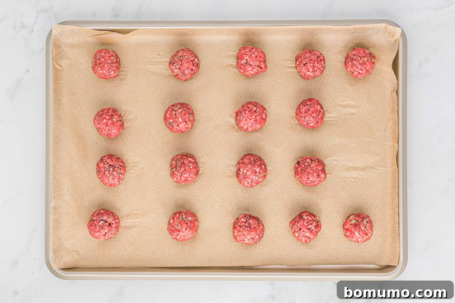 Formed meatballs neatly arranged on a sheet pan, ready for the oven.