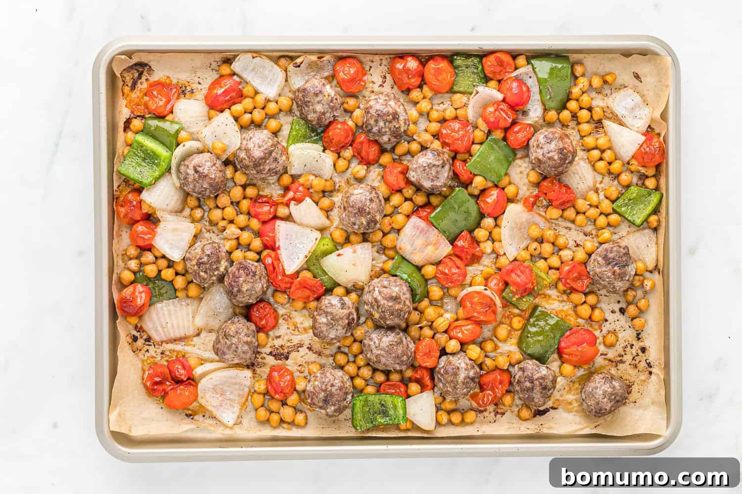 Cooked Moroccan meatballs and roasted vegetables on a sheet pan, fresh out of the oven.