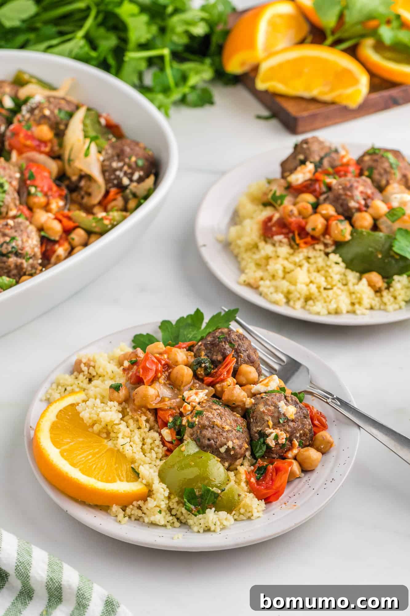 Plated couscous and meatballs with a wedge of orange, garnished with fresh herbs.