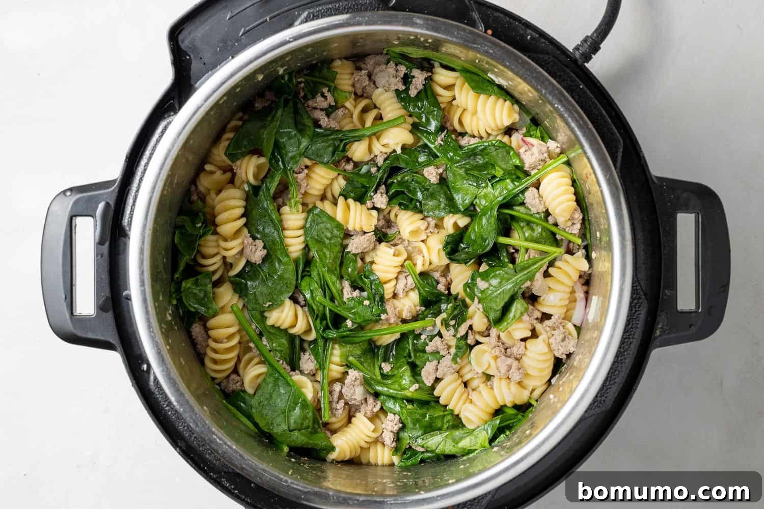 Spinach on top of ground chicken and pasta in an instant pot.
