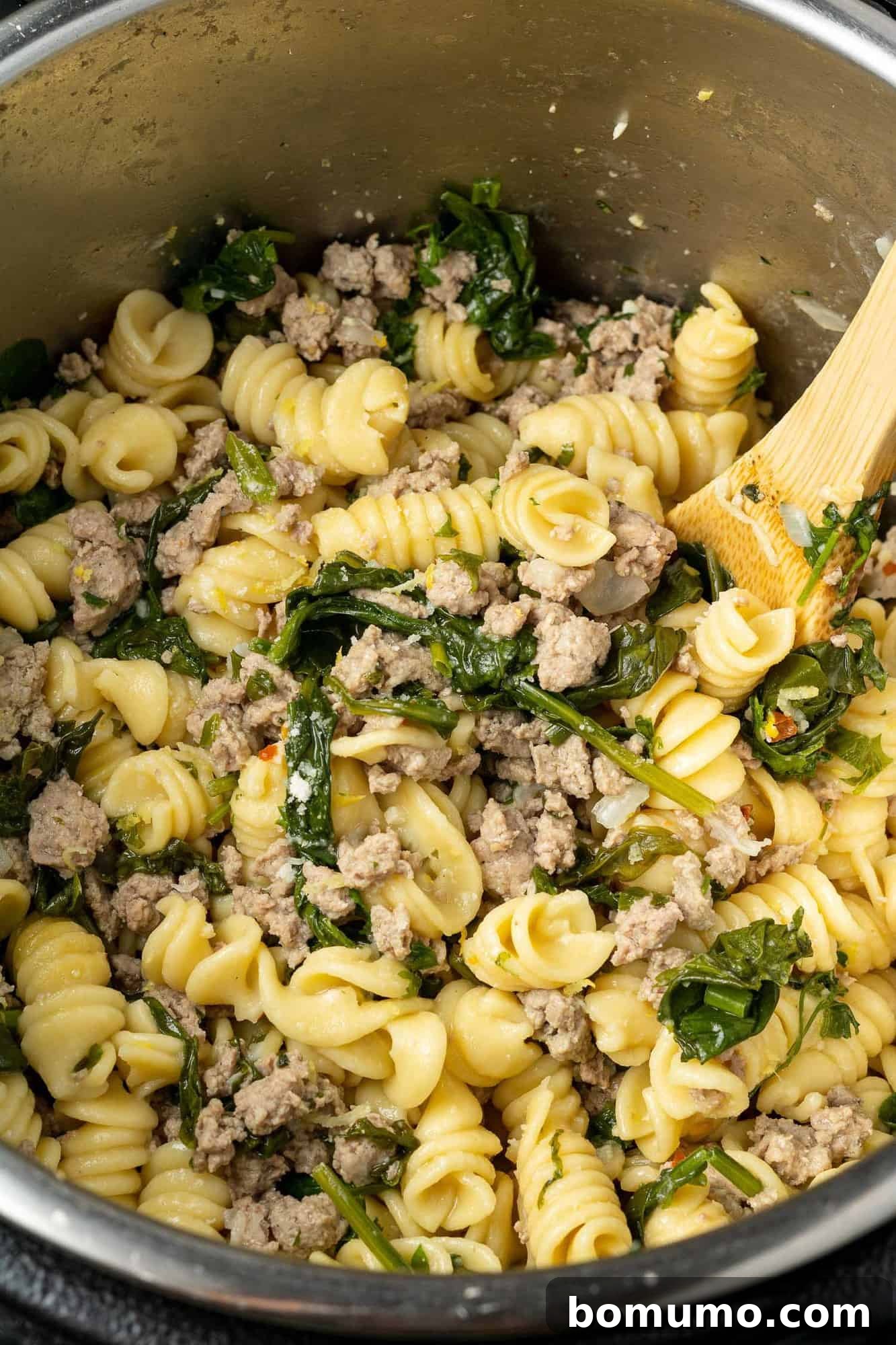 Instant pot filled with pasta, spinach, ground chicken, and a wooden spoon.