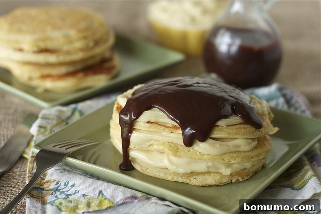 Pancakes on plate with cream and ganache, with plain pancakes in background and pitcher of ganache.