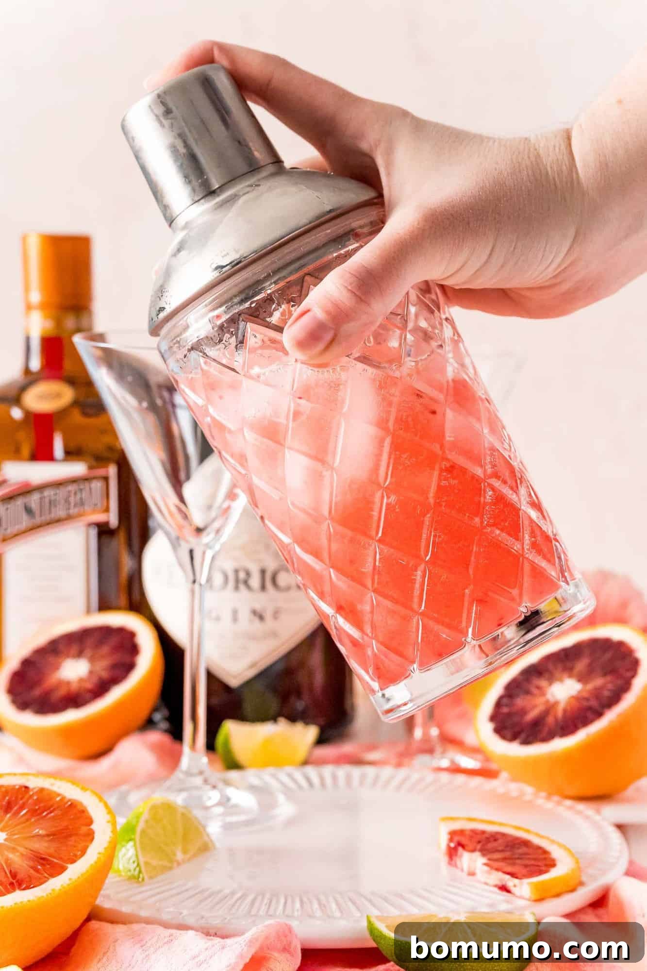 Blood Moon Martini 5 A hand confidently shaking a cocktail shaker, filled with a beautiful pinkish liquid and ice, preparing the martini.