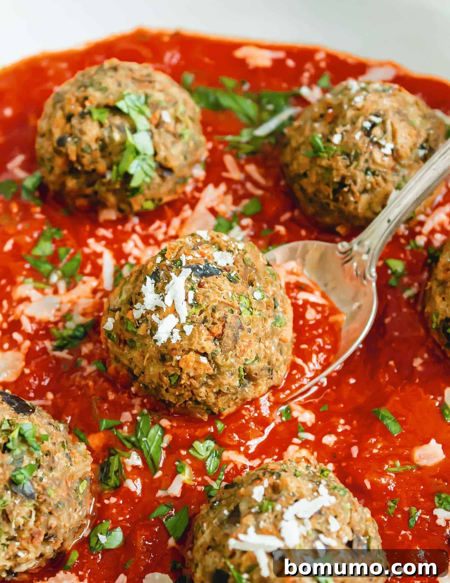 Close up of an eggplant meatball on a spoon, in sauce.