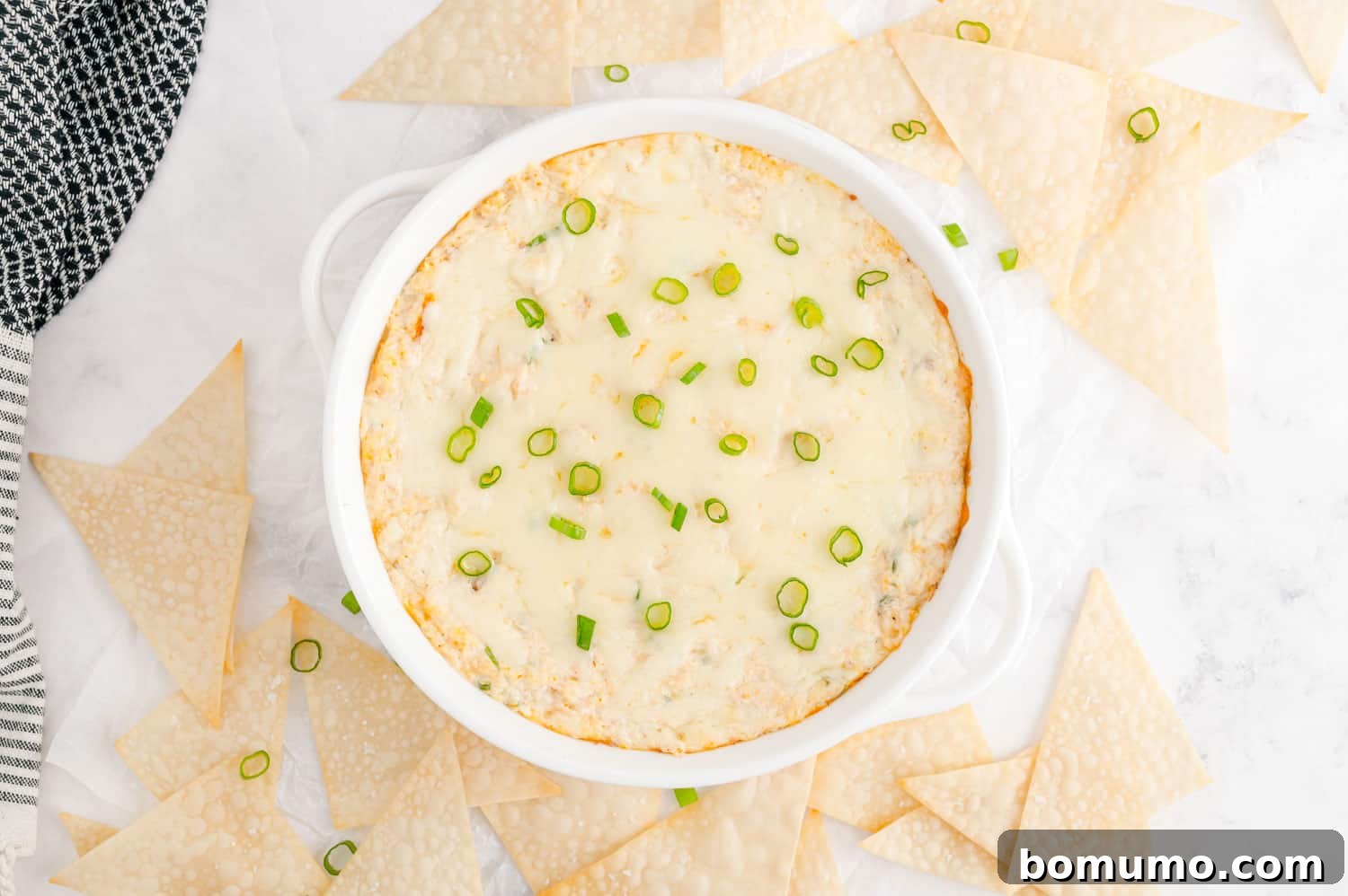 Dip, garnished with green onions, surrounded by wonton triangles.