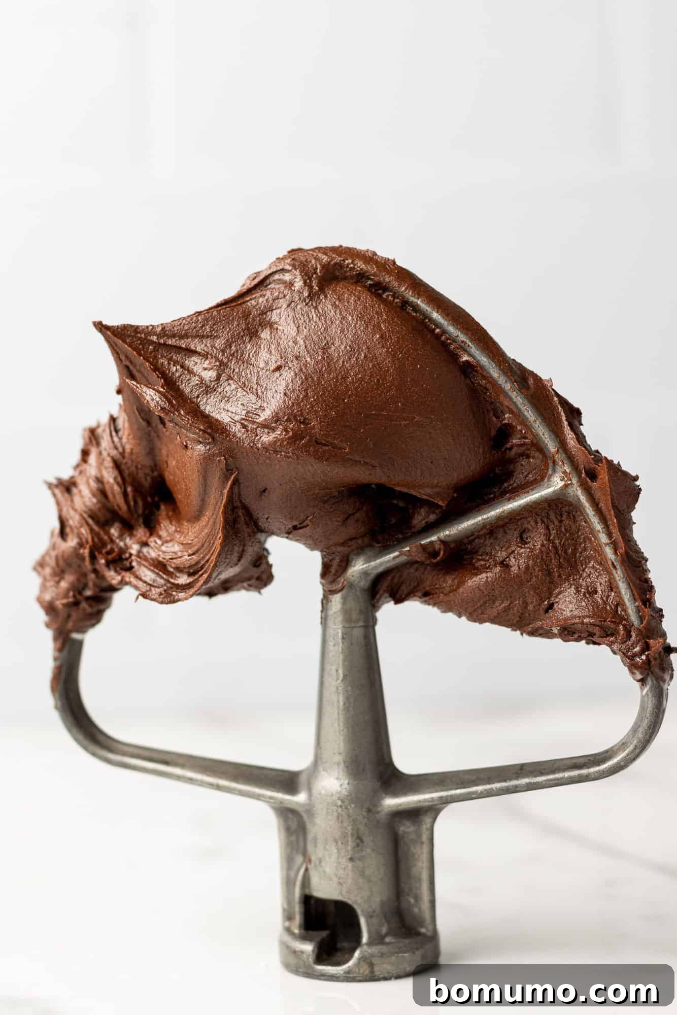 Chocolate buttercream frosting on a mixer beater, showing its smooth, rich texture.