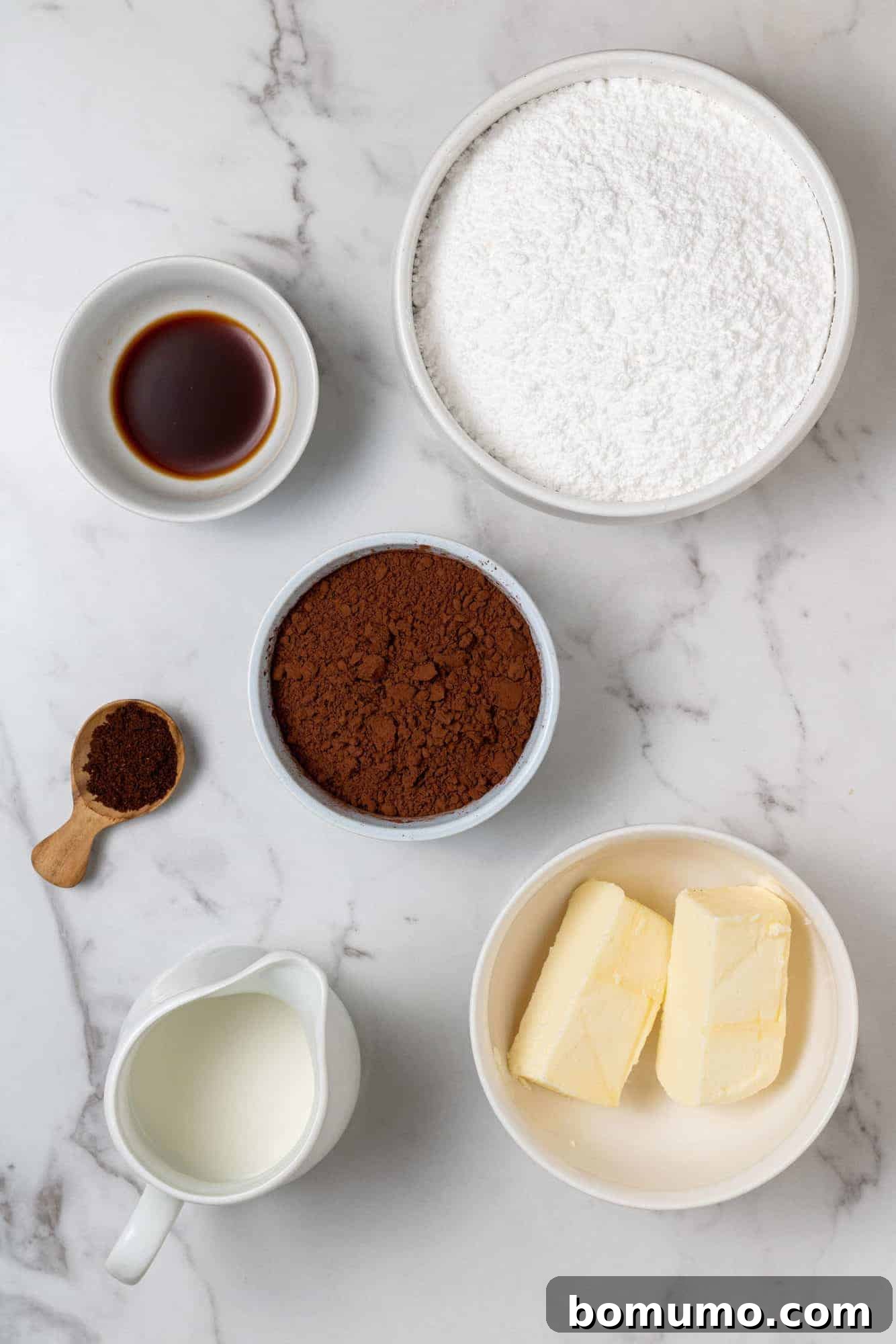 Overhead view of all ingredients needed for chocolate buttercream: powdered sugar, cocoa powder, softened butter, milk, espresso powder, and vanilla extract, neatly arranged.