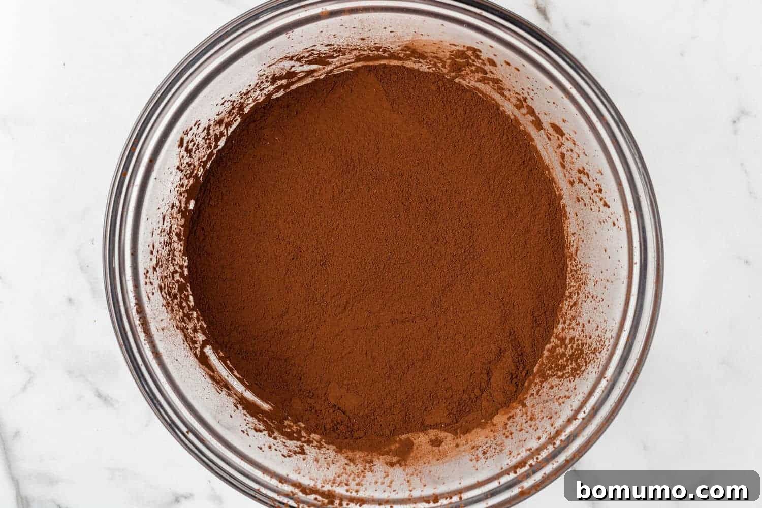 Cocoa powder in a clear glass mixing bowl, ready to be combined with other ingredients.