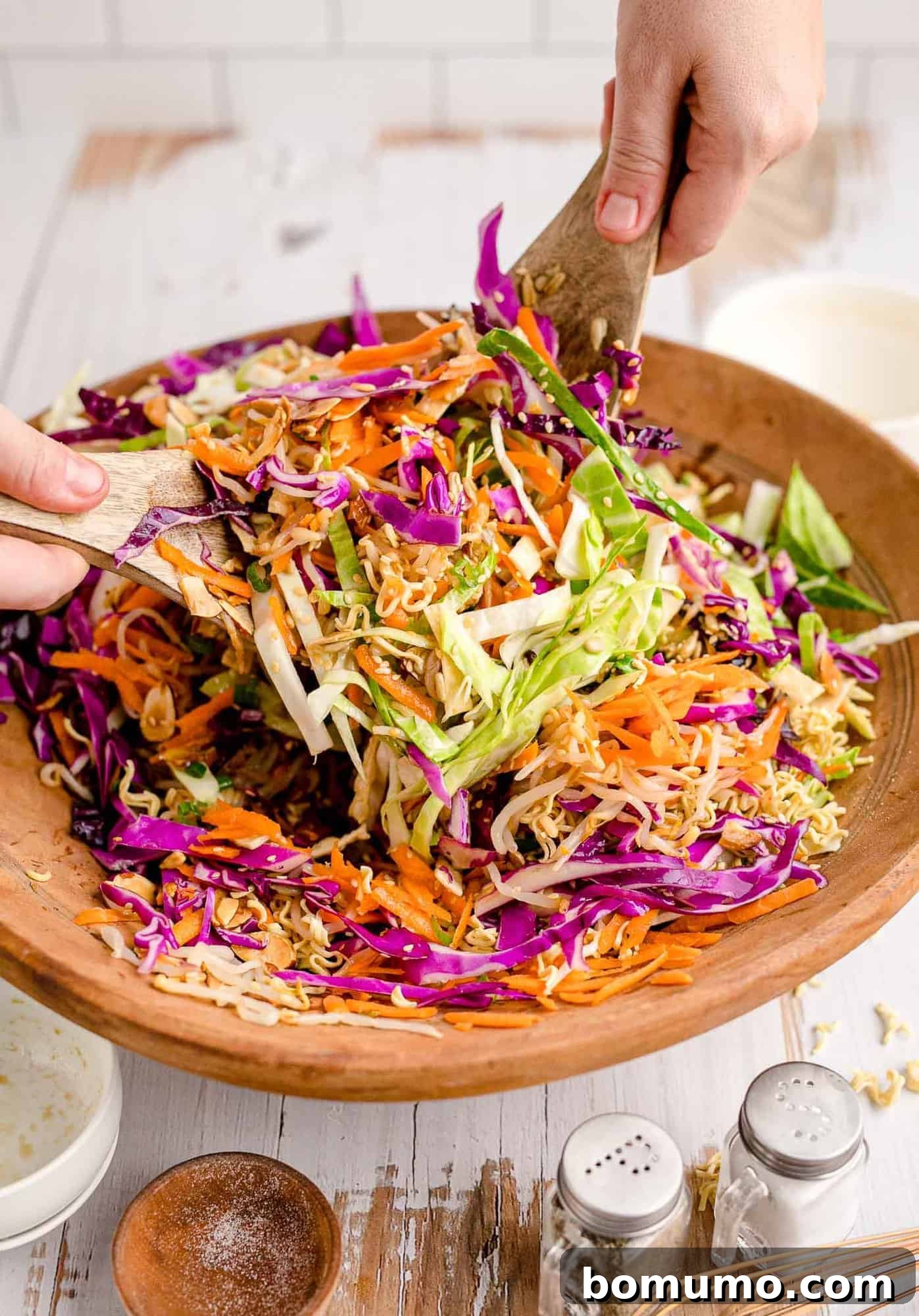 Large salad in a wooden bowl being tossed with handheld salad tongs, showing the generous quantity and fresh ingredients.