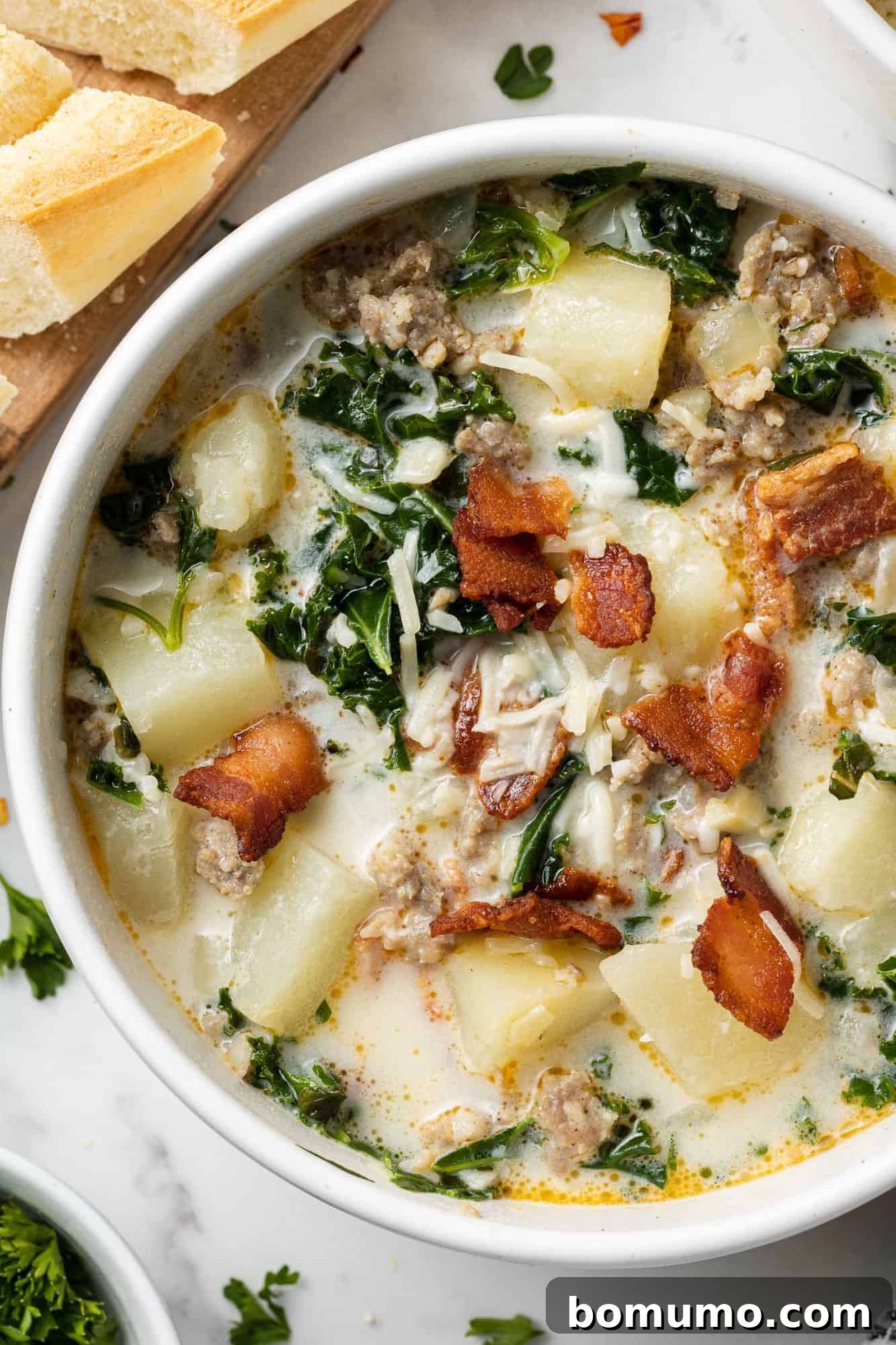Overhead view of zuppa toscana soup in a white bowl garnished with crispy bacon, showcasing its rich, creamy texture and vibrant ingredients.
