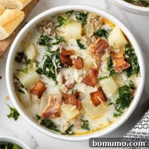 Overhead view of Zuppa Toscana soup in a white bowl garnished with crispy bacon, highlighting its rich, creamy texture and vibrant ingredients.