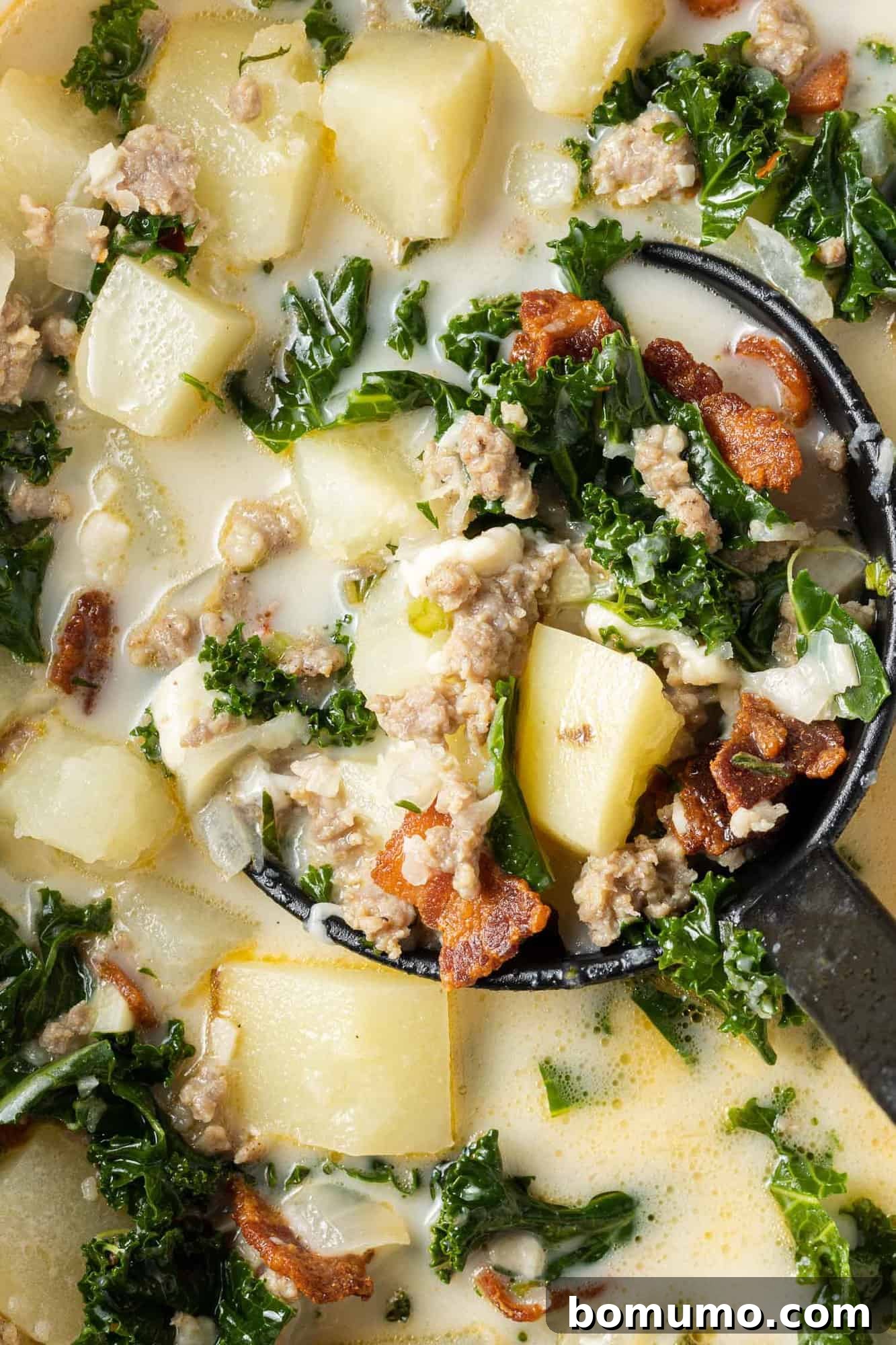Creamy soup with kale, sausage, and potatoes shown in a ladle, highlighting the rich texture and colorful ingredients.