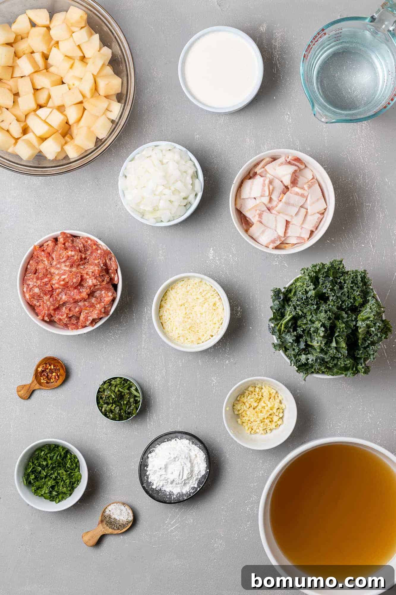 Overhead view of various fresh ingredients for Zuppa Toscana: Italian sausage, russet potatoes, fresh kale, garlic, and onions, neatly arranged.
