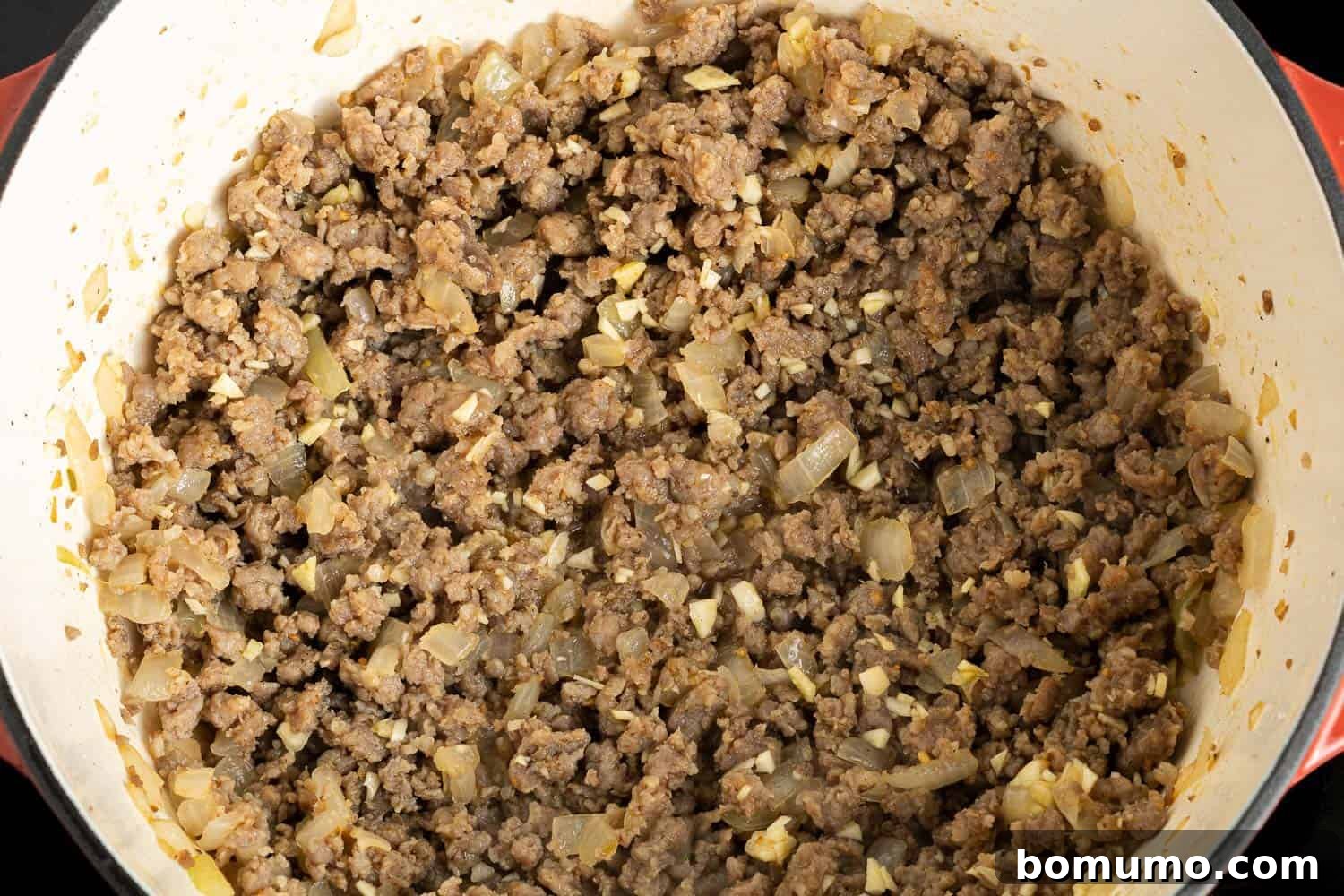 Browned Italian sausage crumbles mixed with soft, translucent onions and fragrant garlic in a large pot.