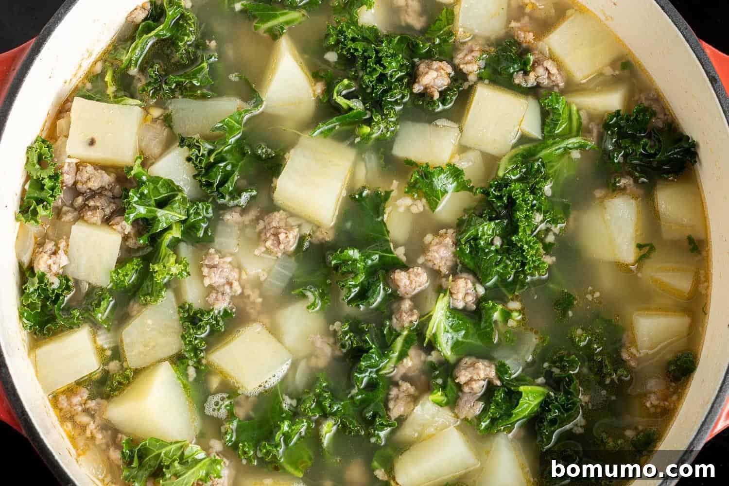 Fresh kale leaves added to the simmering Zuppa Toscana, mingling with the sausage and potatoes in a savory broth, ready to soften.